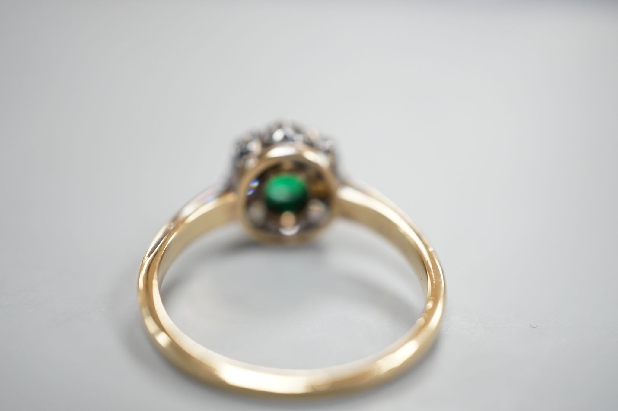 A yellow metal, emerald and diamond set oval cluster ring, size M/N, gross weight 3.1 grams.